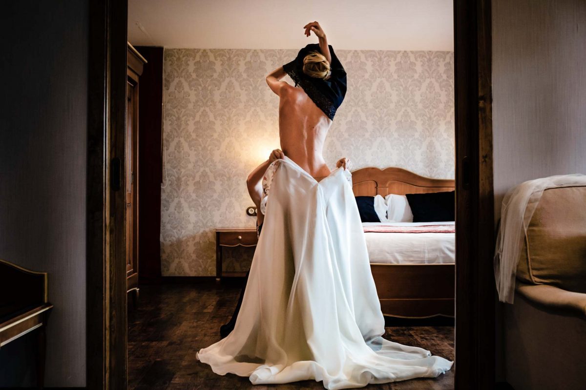 Foto boda sensual novia subiéndose el vestido de espaldas en una habitación lujosa y estilo clásico